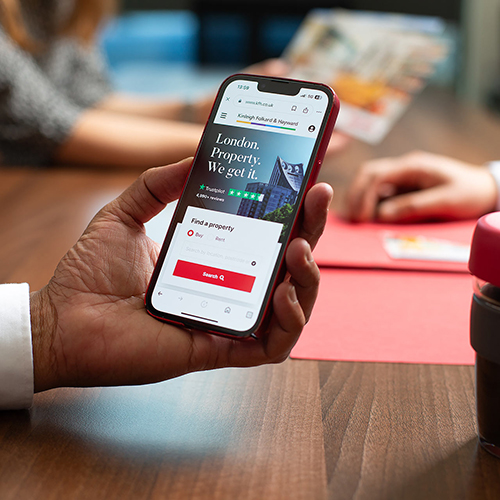 Close up of a male hand holding an iPhone screen showing the KFH website